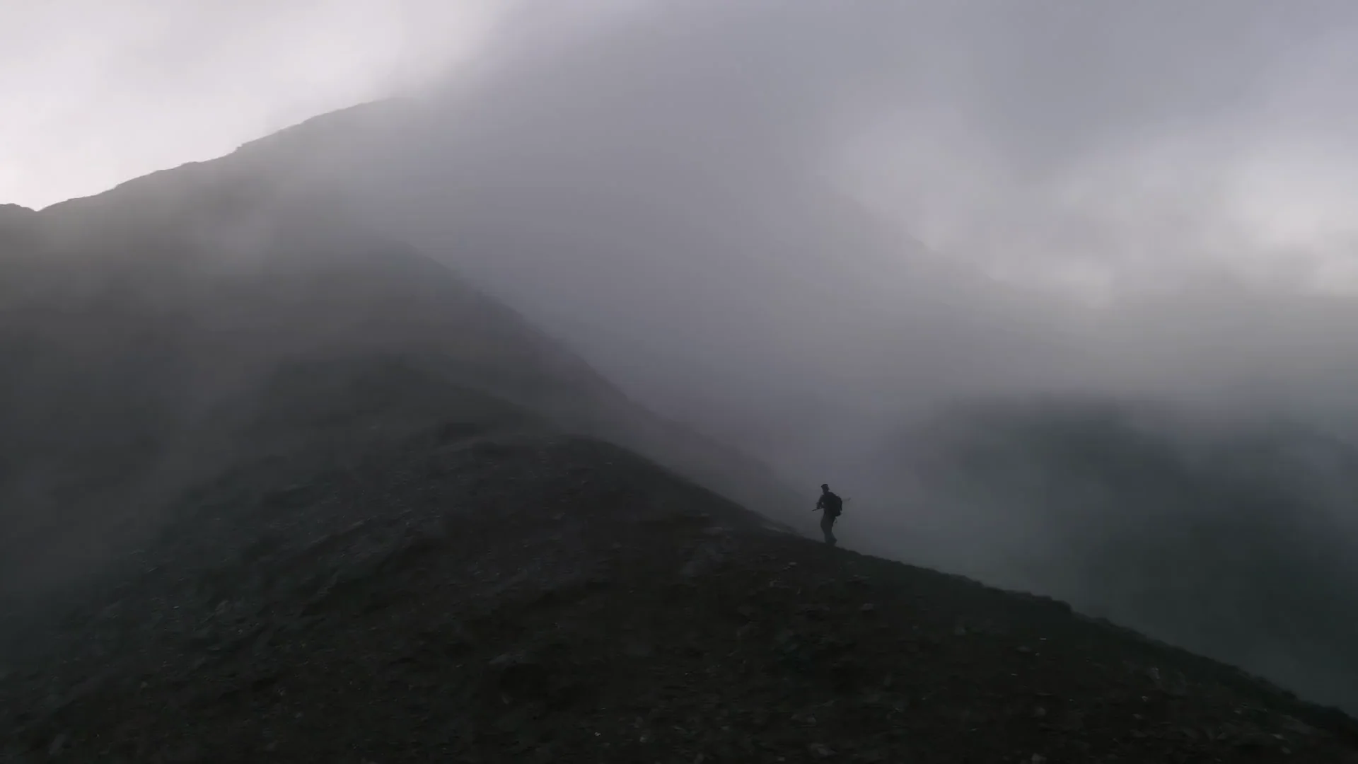 A lone hiker on a mist-covered mountain ridge.